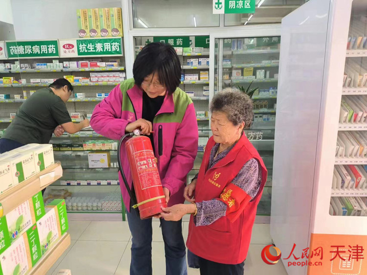 一位热心的“河西大姐”(右)在药店帮助工作人员检查灭火器。人民网记者 孙翼飞摄
