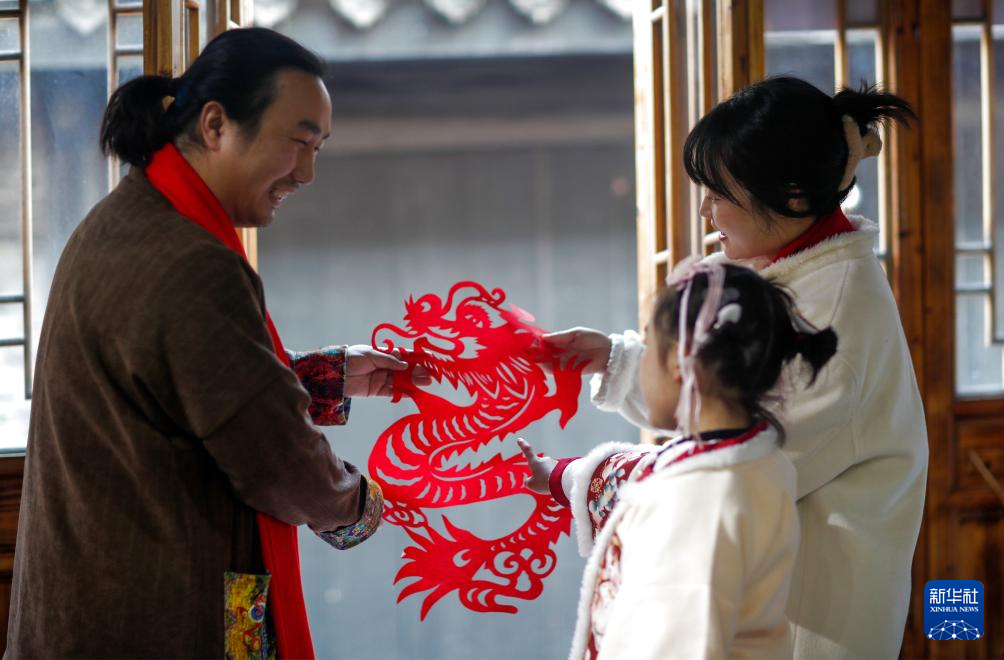 1月11日，在江苏省兴化市昭阳街道北门街区，民间艺人（左）向社区居民介绍“龙”形剪纸作品。
进入农历腊月，春节日益临近，人们忙着购年货、写春联，红红火火迎新春。
新华社发（周社根摄）