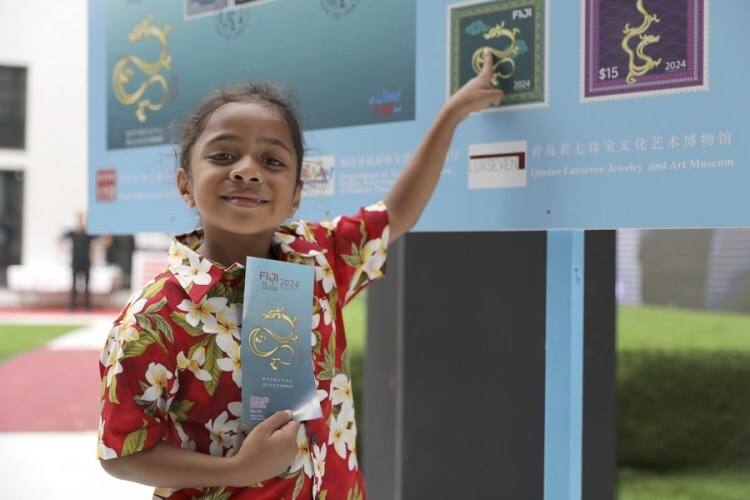 A Fijian child poses for photos with a billboard introducing the Year of Dragon stamps at a launching ceremony held in Nausori, Fiji, Feb. 3, 2024. (Photo by Sang Qinlong/Xinhua)
