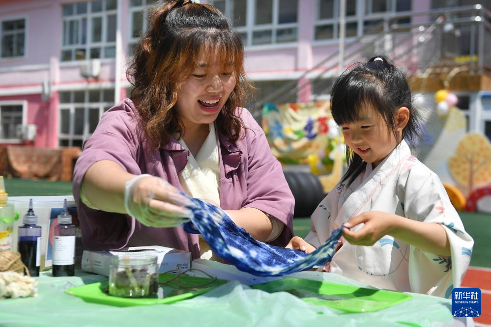 5月29日，小朋友在山东省青岛市市南区新世纪幼儿园迎“六一”活动上跟随老师学习非遗扎染。