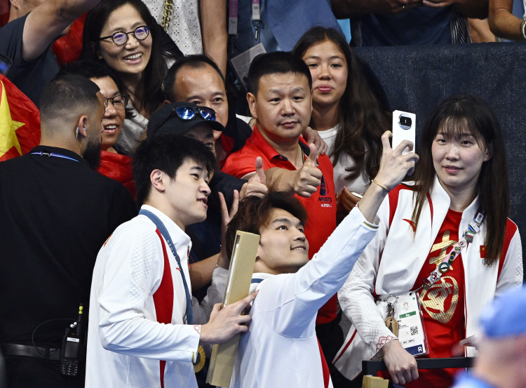 Gold medalists Pan Zhanle (L,front) and Xu Jiayu of Team China take selfies with spectators after the victory ceremony for the men's 4 x 100m medley relay of swimming at Paris 2024 Olympic Games in Paris, France, on Aug. 4, 2024. (Xinhua/Wang Peng)