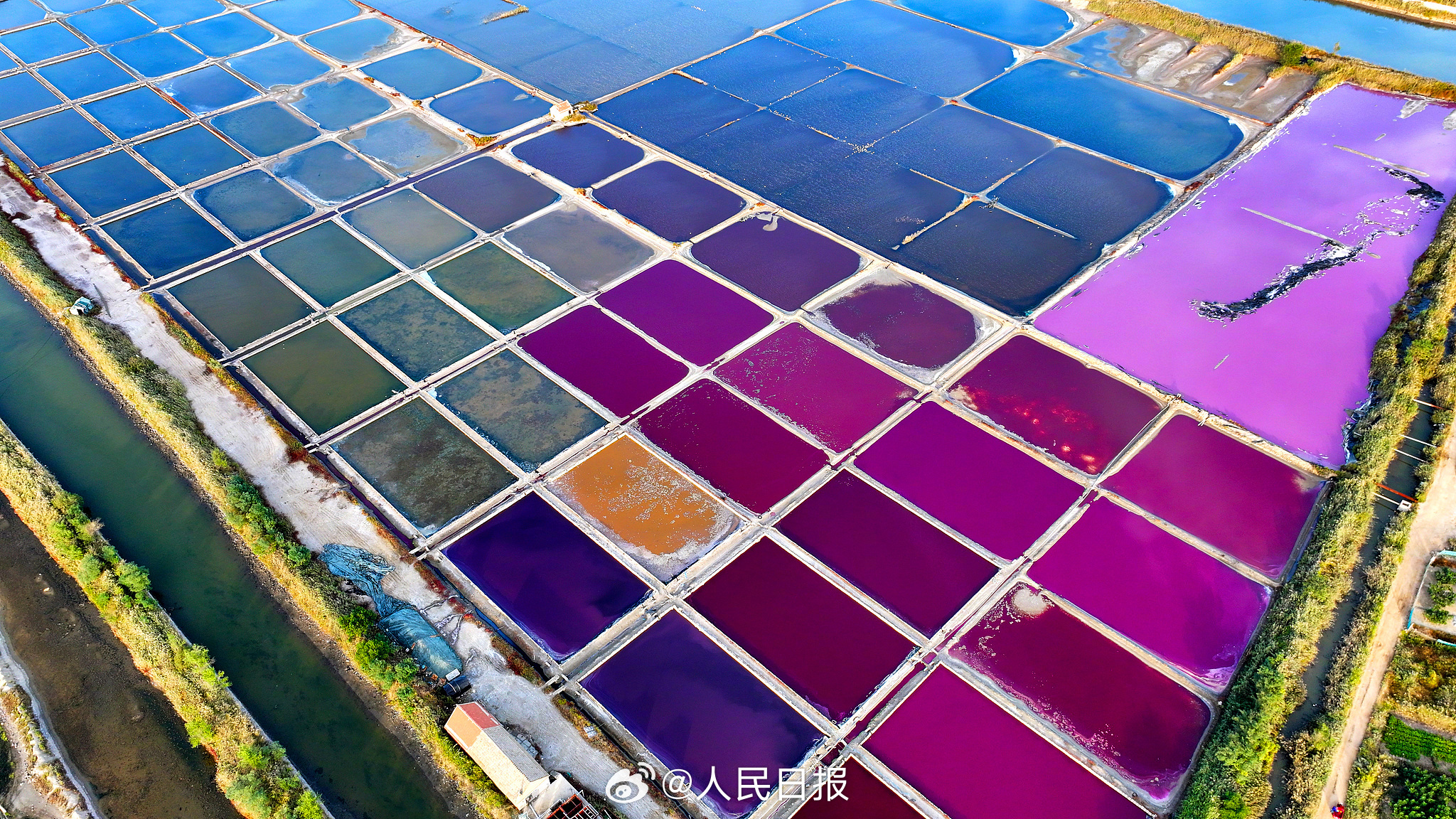 近日，山东荣成，港西镇朝阳港一处盐田，呈现出高饱和度色彩，像是被大自然打翻的调色盘，又如同神秘的大地呈现的一片艺术画布，形成了一道靓丽的风景线。