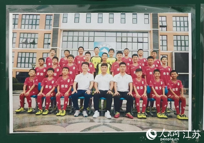 李世恩(上排左四)在淮安工业园区实验学校05-06组足球队的合影张贴在教练室墙上,照片中多名球员正效力于“苏超”淮安队。 人民网 鞠峰摄